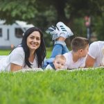 Happy family lying on grass with RV in the background, enjoying a sunny outdoor picnic.